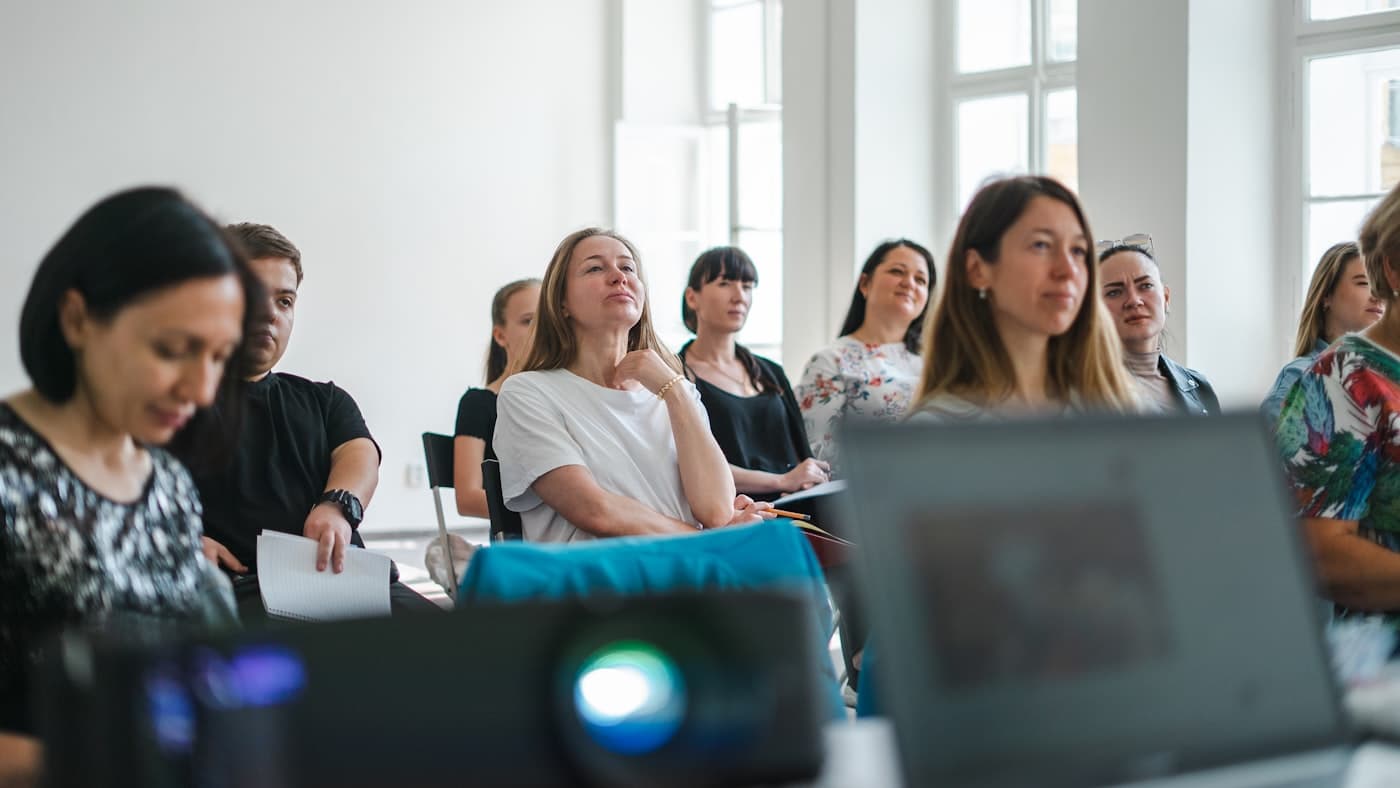 Un groupe de personnes assises dans une salle claire, écoutant une présentation